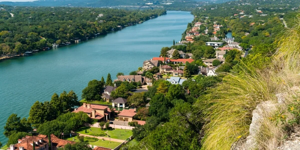 Stunning aerial panorama of turquoise Lake Travis nestled between limestone bluffs, with luxury hillside estates anchoring emerald-canopied terrain.