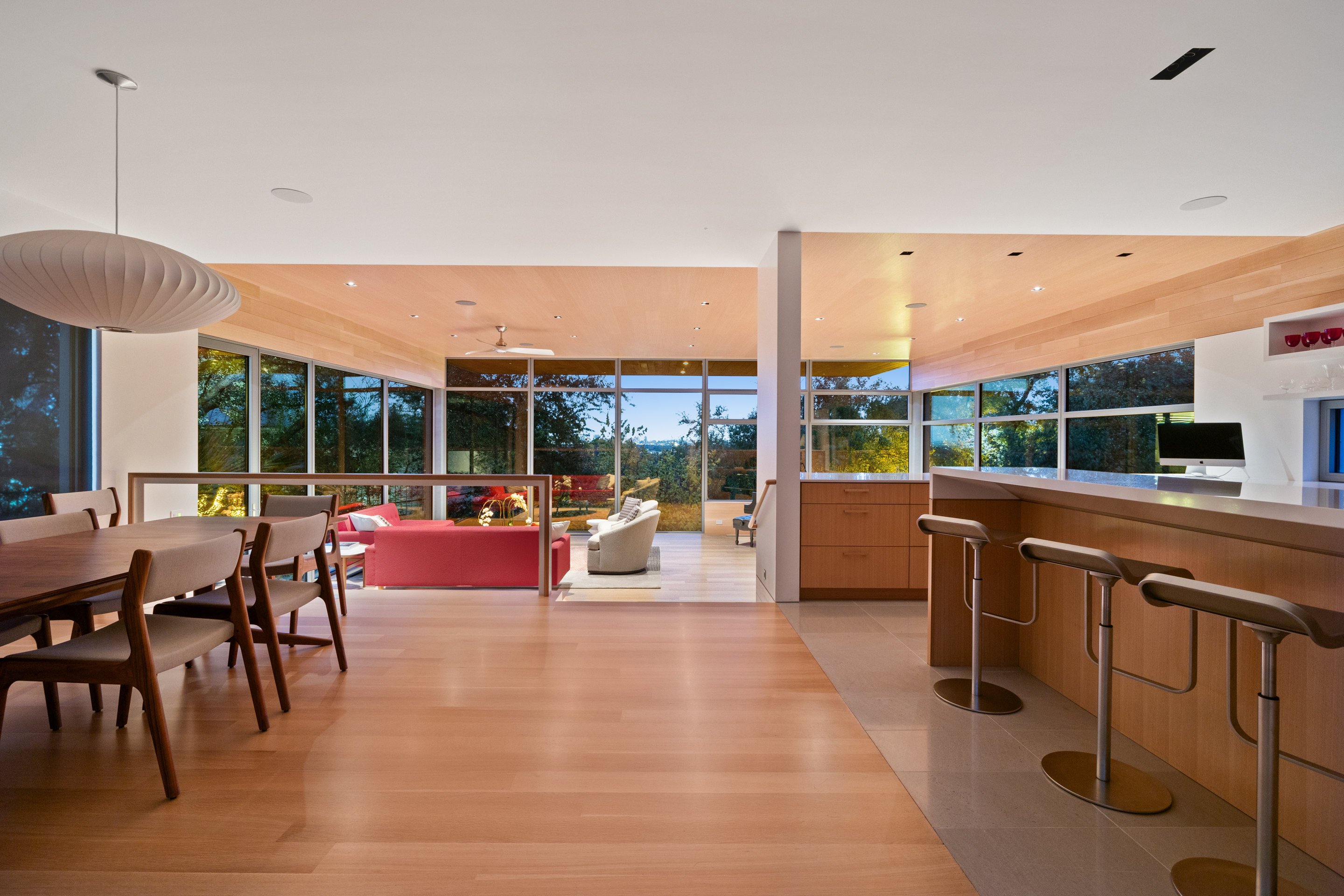 Open plan living, dining, and kitchen with acoustic wood ceiling panels and wall-to-wall windows