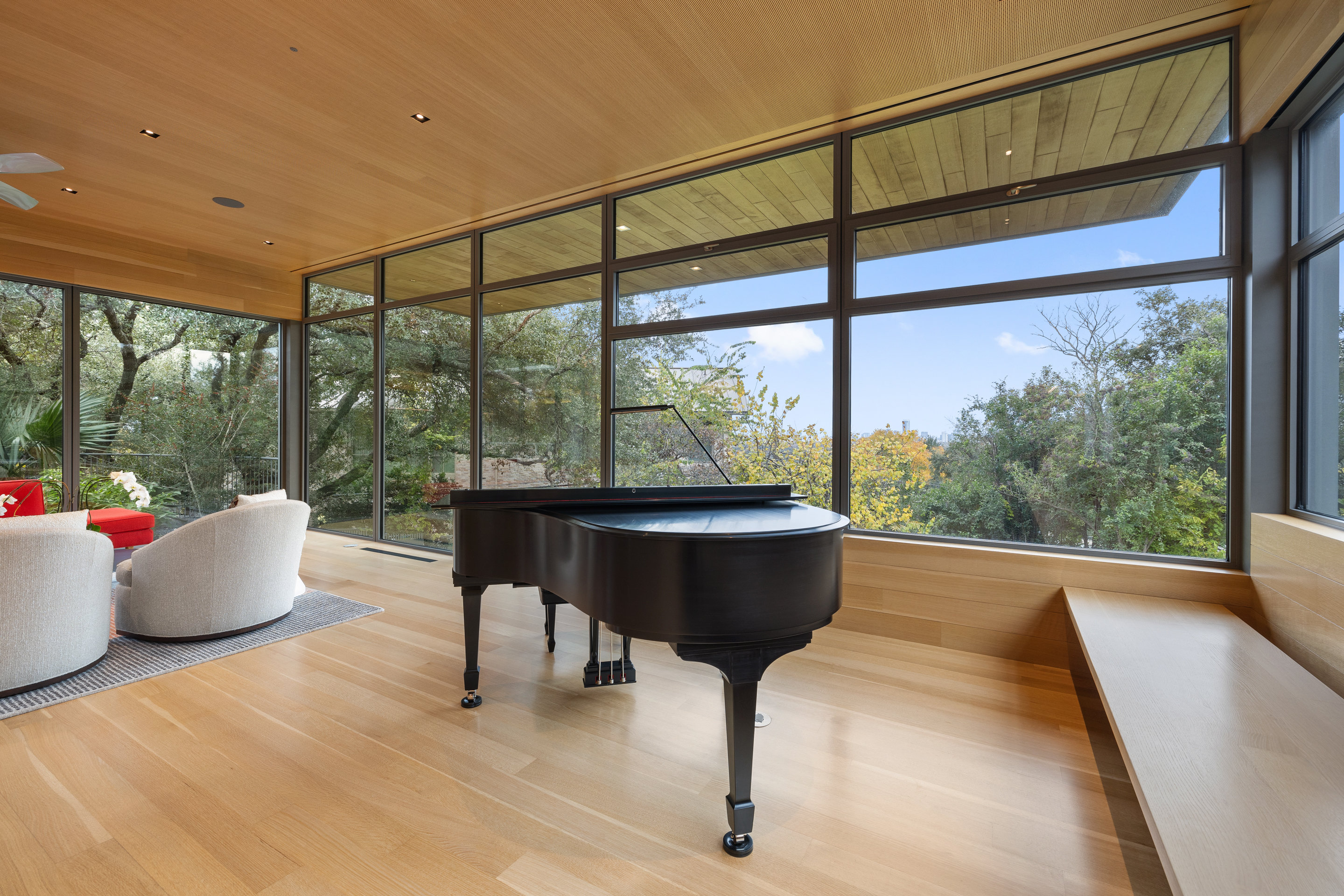 Piano room with floor-to-ceiling windows and wood-paneled ceiling overlooking tree canopy