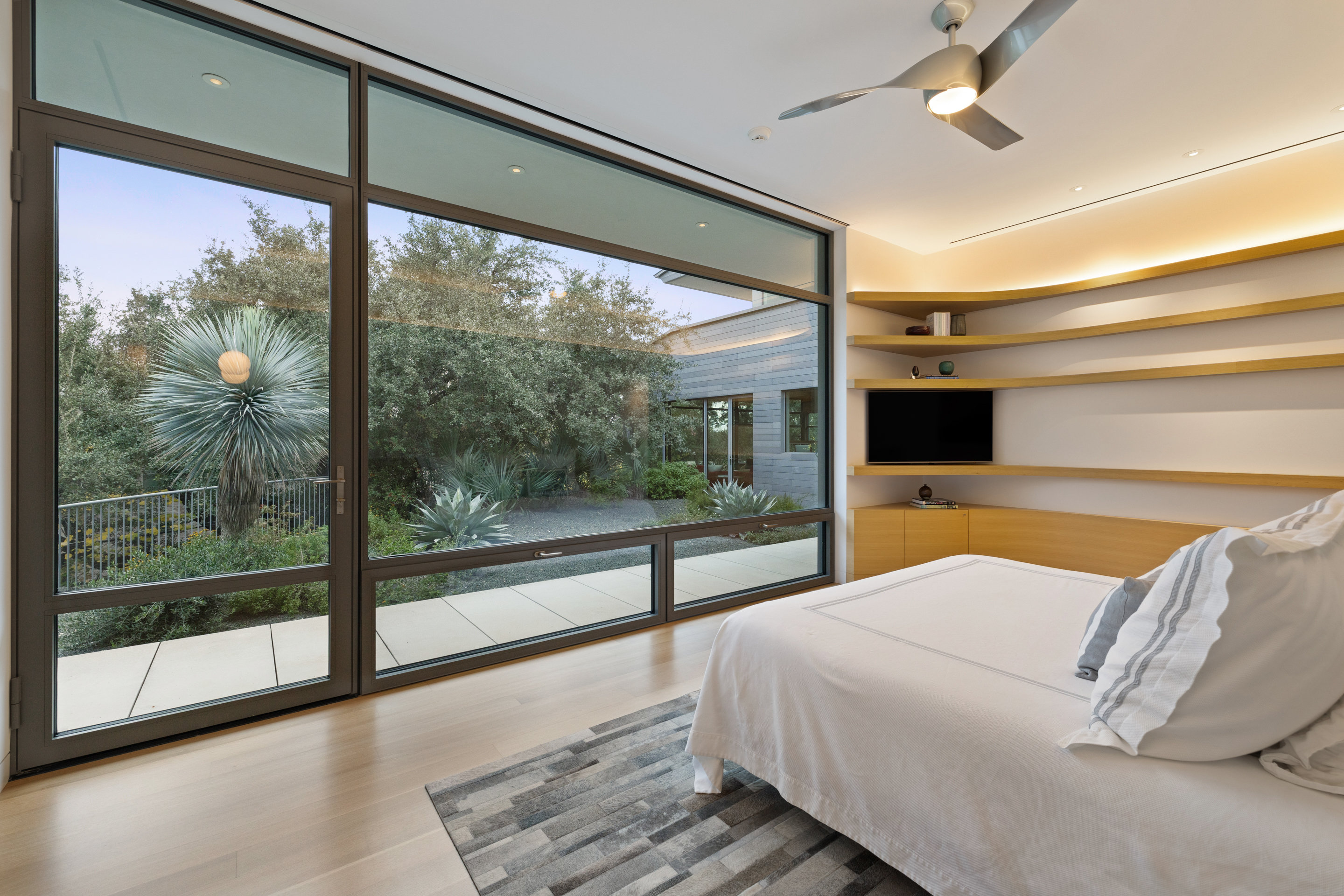 Primary bedroom with floor-to-ceiling glass, courtyard garden view, and built-in shelving