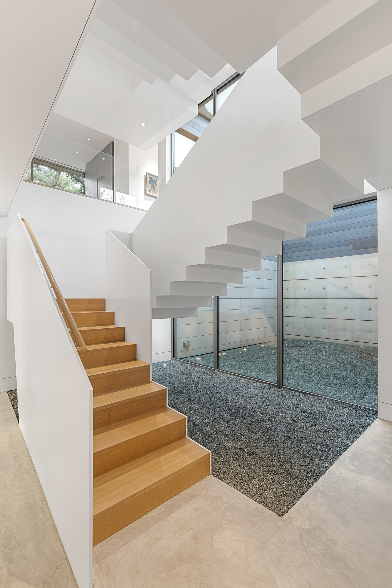 Full three-story stairwell view with glass wall, gravel courtyard, and skylight above