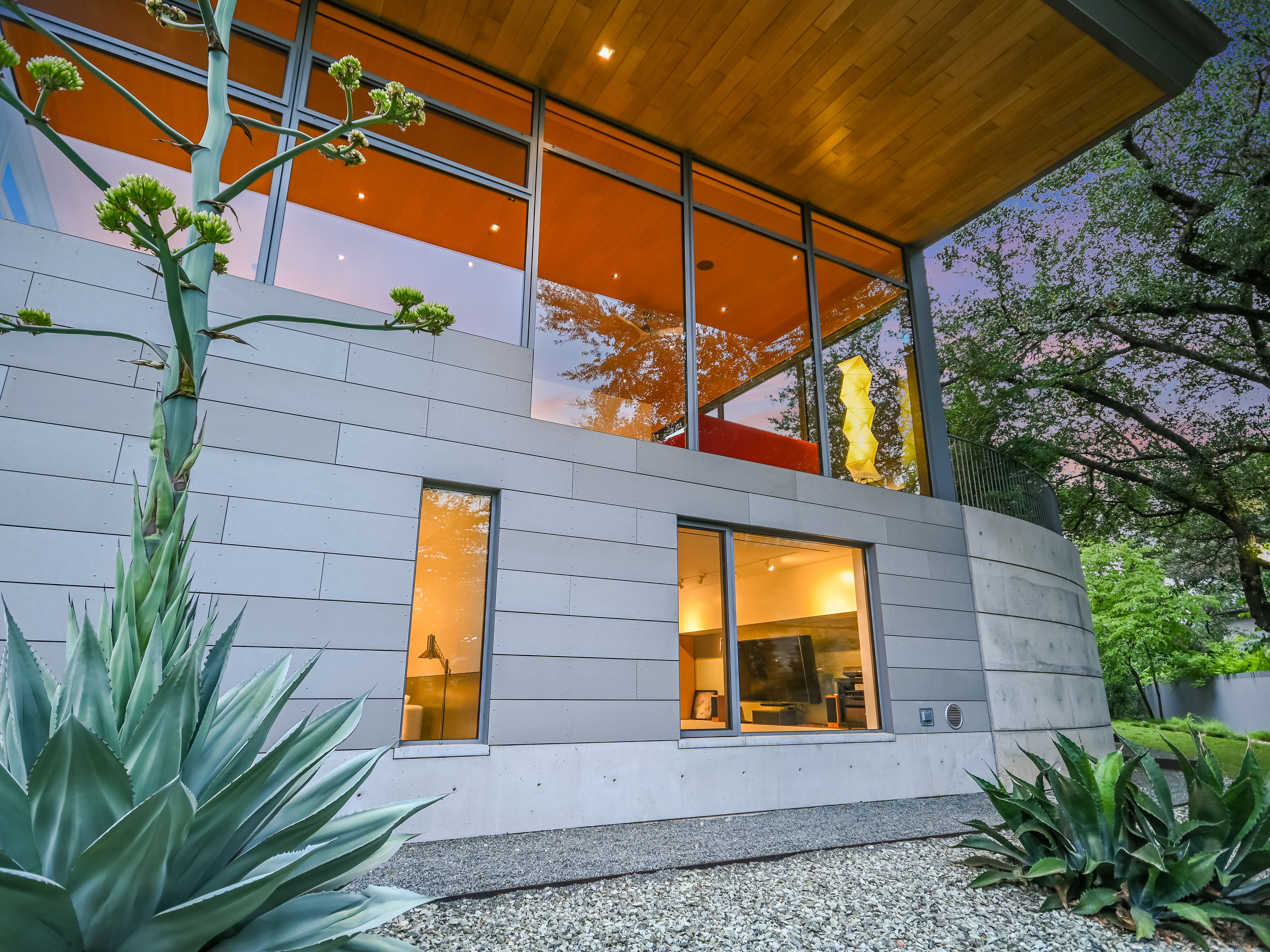 Back of house with illuminated interiors seen through floor-to-ceiling glass