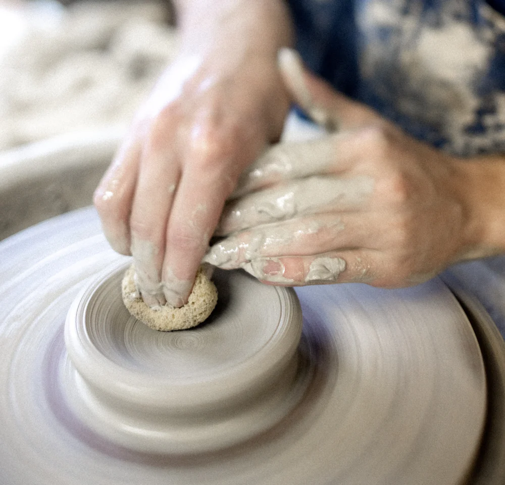 Hands shaping clay on a pottery wheel.