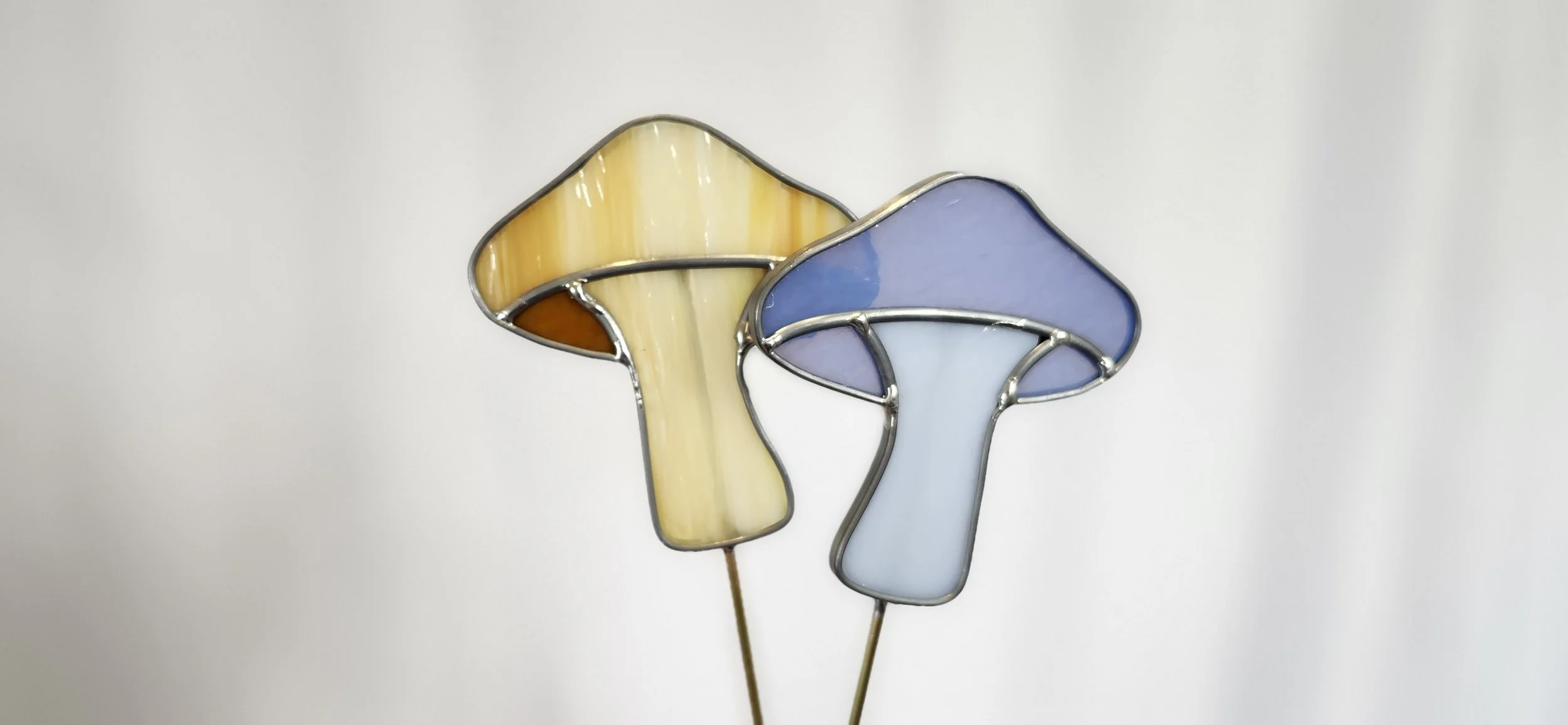 Two stained-glass mushroom pieces on slender stakes.
