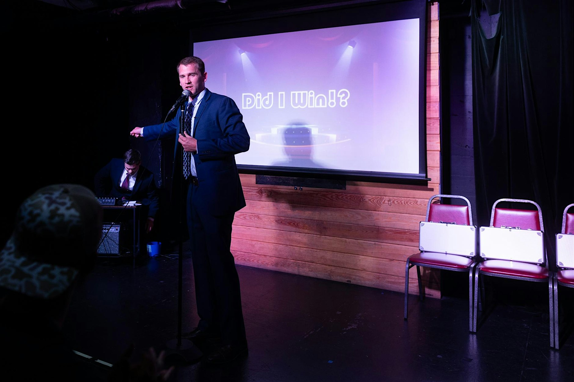 A presenter with a microphone beside a game-show screen.