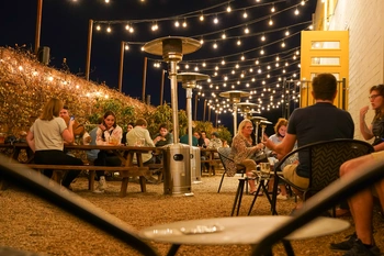 Guests at long tables under string lights and patio heaters at night.