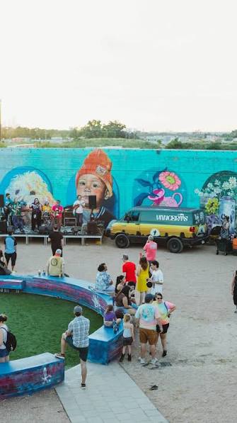 A crowd gathers in front of a long, brightly painted mural wall at an outdoor art event.
