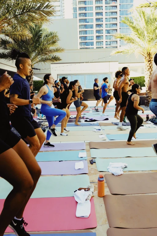 A group exercising on yoga mats on an outdoor deck with palm trees and high-rise buildings behind them.
