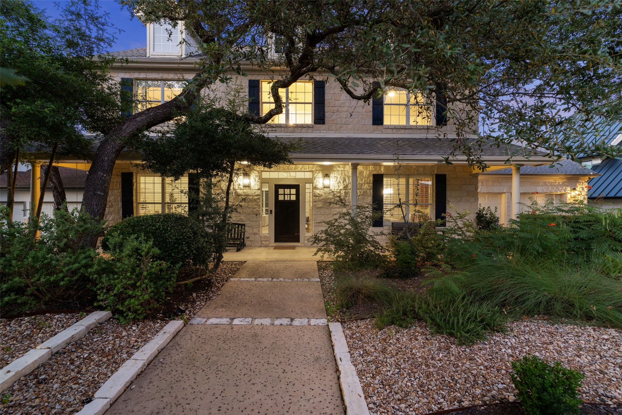 The front walk and stone facade of 6213 Edwards Mountain Cove at dusk, under large live oaks.