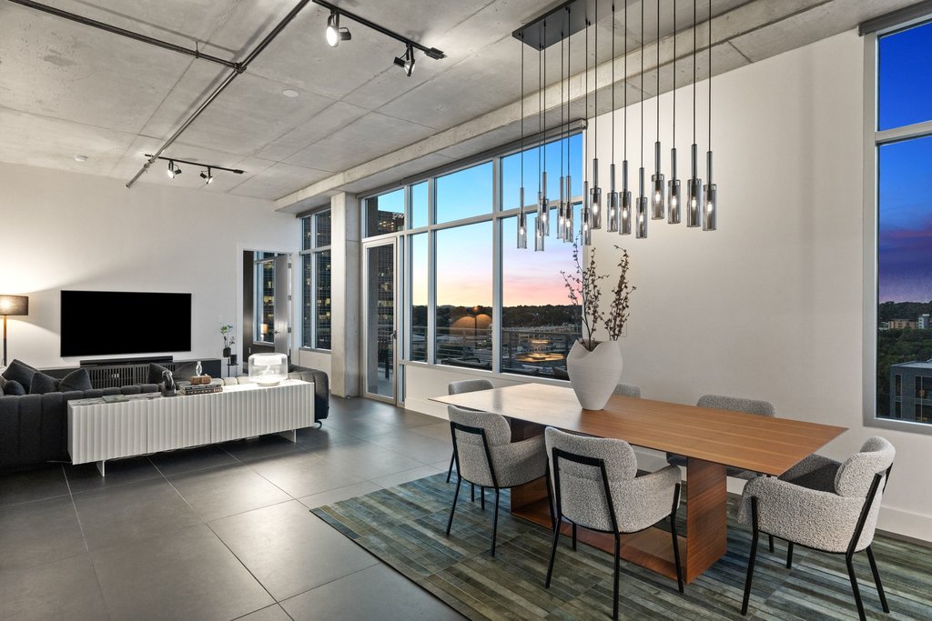 The living and dining area of Unit 1004 at 800 West 5th Street, with floor-to-ceiling windows at dusk.