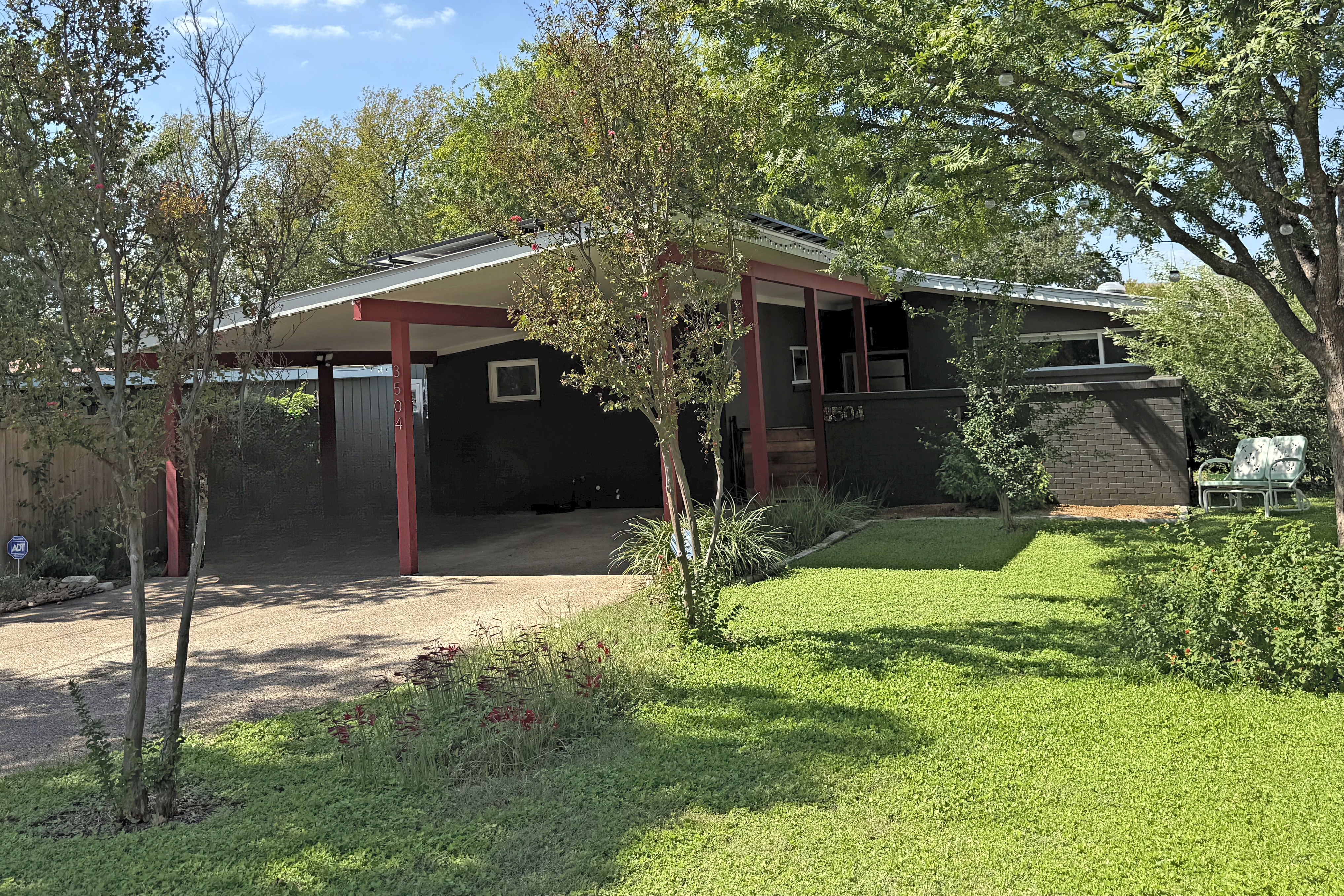 3504 West Avenue, a low mid-century home with red posts and a carport, behind a green lawn and young trees.