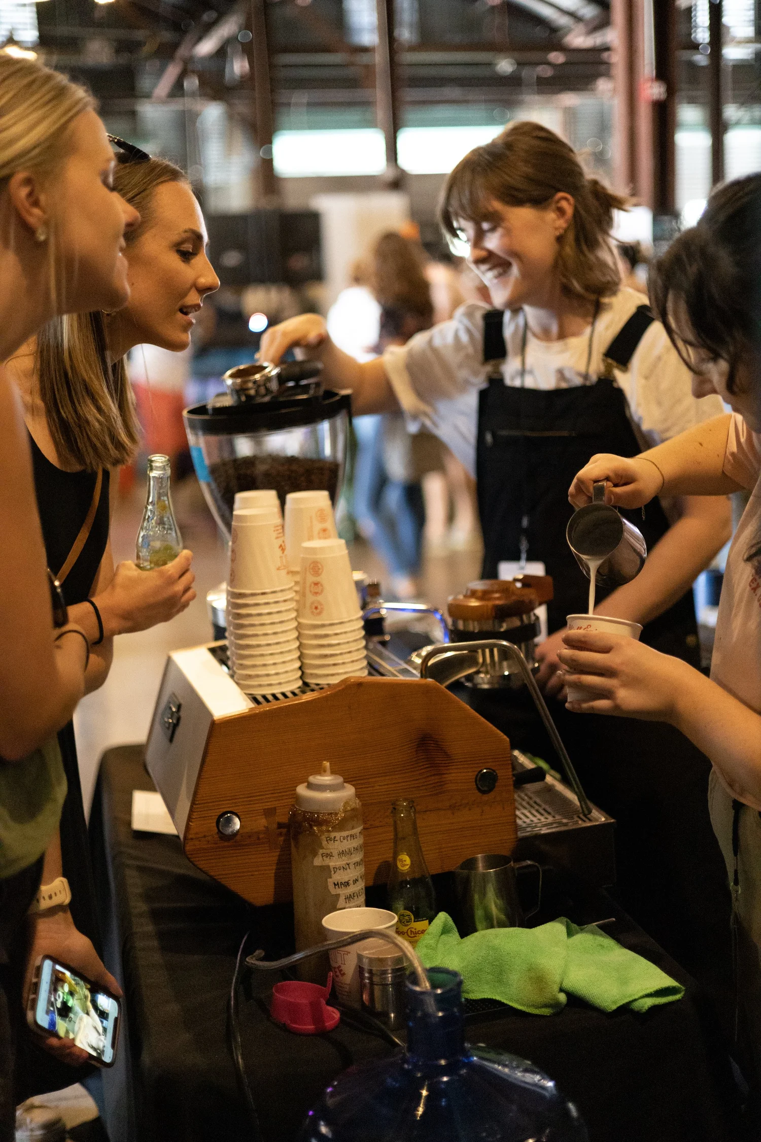 A barista pours coffee for festival guests at a table stacked with paper cups.