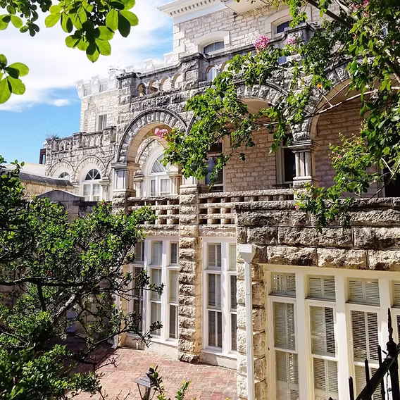 The limestone facade of Chateau Bellevue, with arched windows and a stone balustrade framed by green trees.