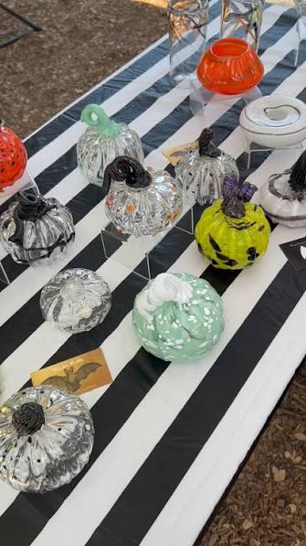 Hand-blown glass pumpkins in clear, green, orange and black glass on a black-and-white striped table.